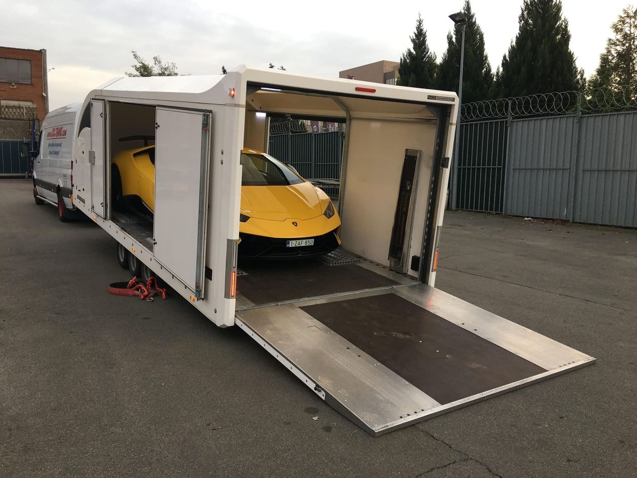 Compacte gesloten JDC-Trans-vrachtwagen met gele Lamborghini Huracán aan boord, oprijplaat uitgeklapt